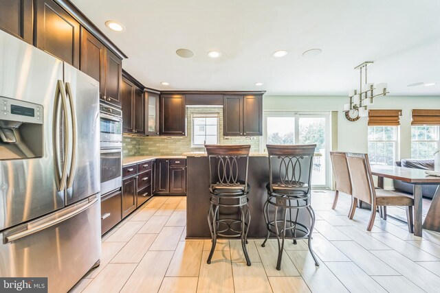 kitchen with dark brown cabinets, a kitchen bar, stainless steel appliances, a kitchen island, and decorative backsplash