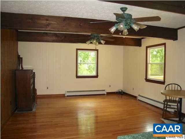 unfurnished room with beam ceiling, wood-type flooring, plenty of natural light, and baseboard heating