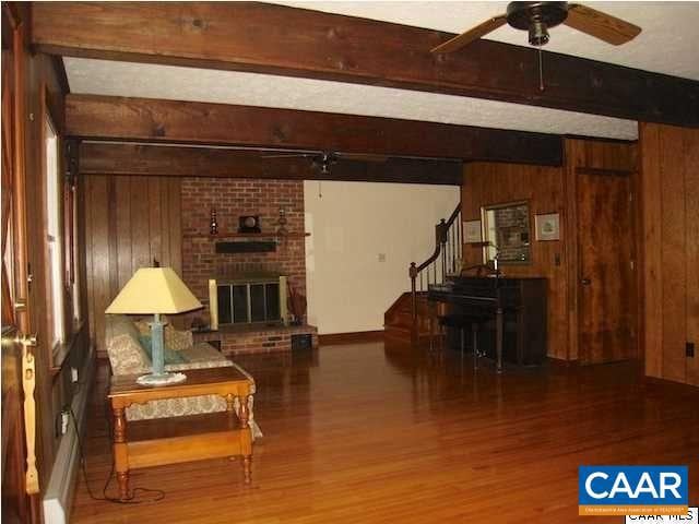 sitting room featuring wood walls, hardwood / wood-style floors, brick wall, beamed ceiling, and a fireplace