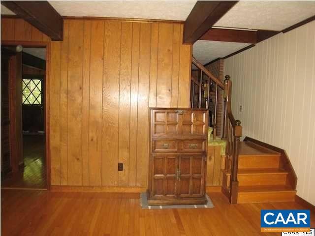 stairs featuring beam ceiling, wooden walls, and wood-type flooring