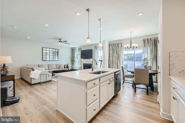kitchen with light countertops, a sink, light wood-style floors, ceiling fan with notable chandelier, and dishwasher