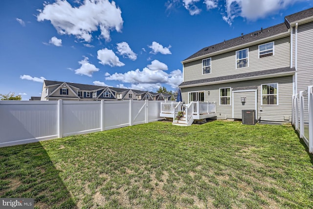 back of property with a fenced backyard, a wooden deck, a yard, and central AC unit