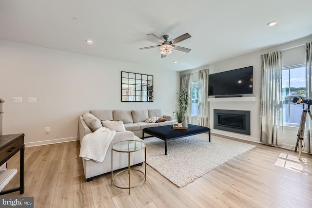 living area featuring a ceiling fan, a healthy amount of sunlight, a glass covered fireplace, and light wood-type flooring
