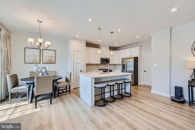 kitchen featuring white cabinets, stainless steel appliances, a sink, backsplash, and light countertops