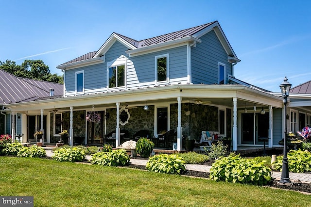 back of house featuring ceiling fan, metal roof, stone siding, a lawn, and a standing seam roof