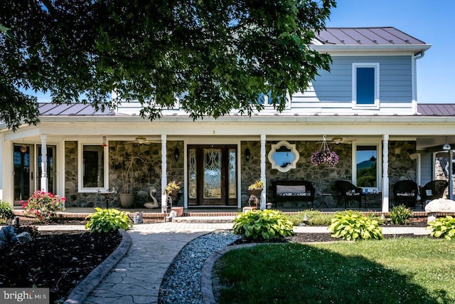 doorway to property featuring stone siding, a standing seam roof, covered porch, and metal roof