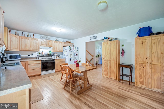 kitchen with a textured ceiling, white appliances, light brown cabinetry, sink, and light hardwood / wood-style floors