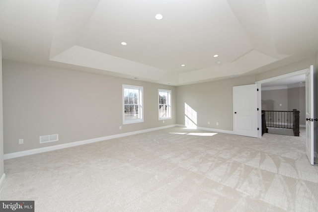 empty room with a raised ceiling and light carpet