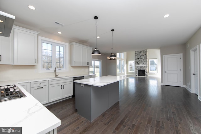 kitchen with a large fireplace, dark hardwood / wood-style floors, a kitchen island, brick wall, and sink