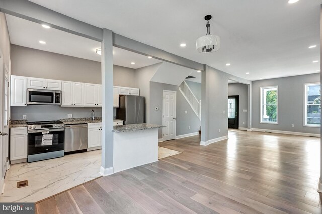 kitchen featuring stainless steel appliances, white cabinetry, light stone counters, light wood-type flooring, and hanging light fixtures