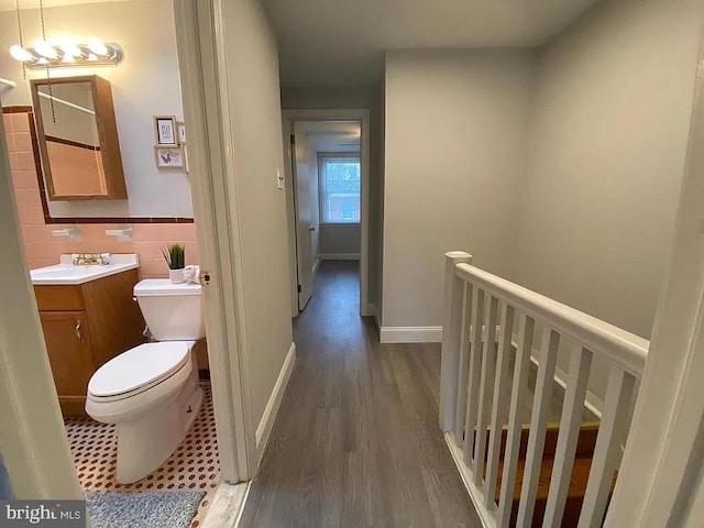 hallway featuring a wainscoted wall, wood finished floors, an upstairs landing, and tile walls