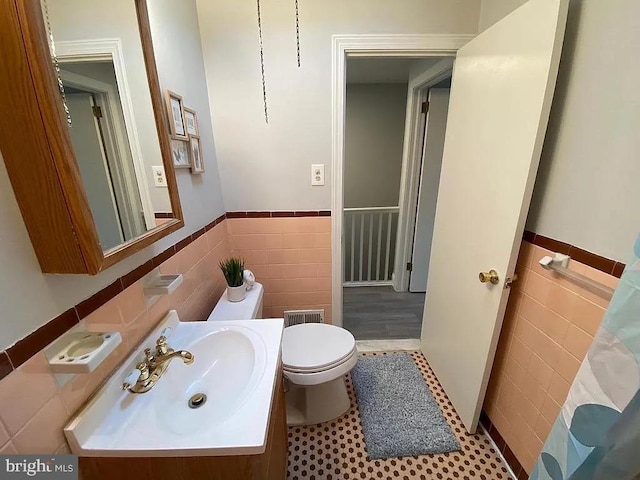 bathroom featuring a wainscoted wall, tile walls, toilet, and vanity