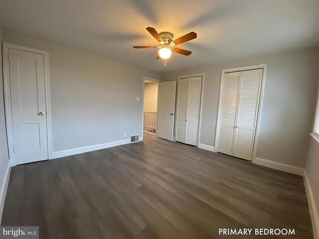 unfurnished bedroom featuring dark wood-type flooring, two closets, and ceiling fan