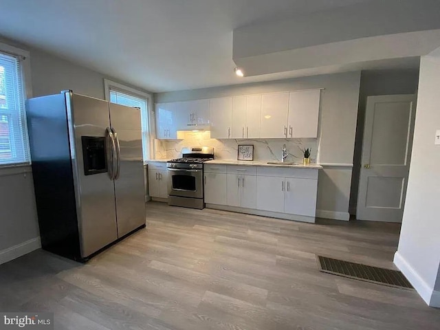 kitchen featuring light wood-type flooring, stainless steel appliances, decorative backsplash, and white cabinetry