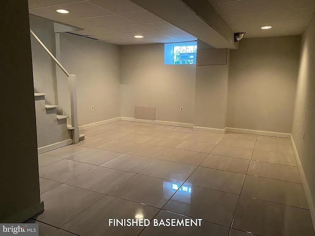 below grade area with a paneled ceiling, stairway, baseboards, and light tile patterned floors