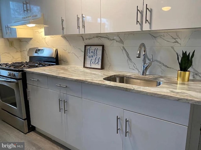 kitchen featuring gas stove, light wood-type flooring, light stone countertops, sink, and decorative backsplash