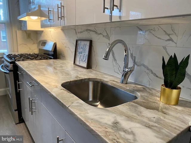 kitchen with backsplash, gas range, light stone countertops, sink, and wall chimney exhaust hood