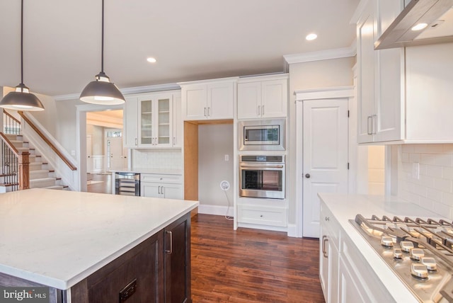 kitchen with stainless steel appliances, hanging light fixtures, glass insert cabinets, white cabinetry, and wall chimney range hood