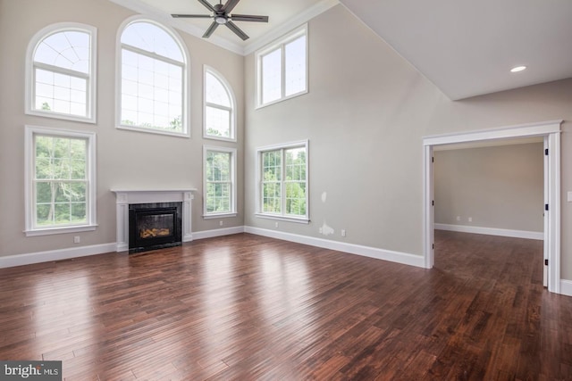 unfurnished living room featuring baseboards, a ceiling fan, a towering ceiling, dark wood-style flooring, and a high end fireplace