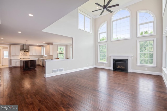 unfurnished living room featuring dark wood-style floors, plenty of natural light, a glass covered fireplace, and visible vents