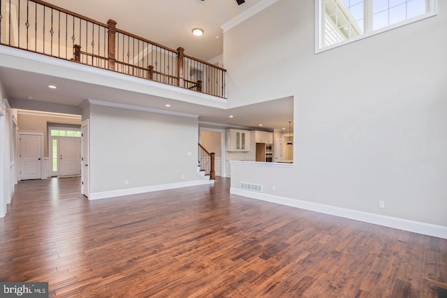 unfurnished living room with baseboards, visible vents, stairway, dark wood-type flooring, and crown molding