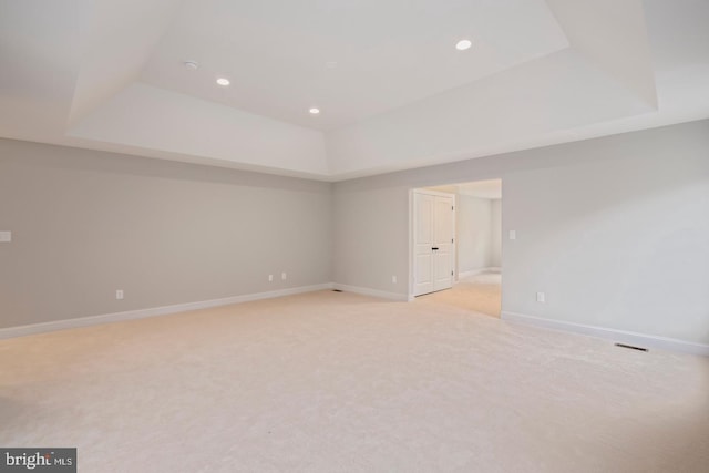 spare room featuring a raised ceiling, light colored carpet, and baseboards