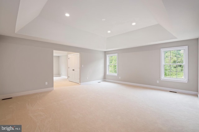 spare room with baseboards, a raised ceiling, visible vents, and light colored carpet