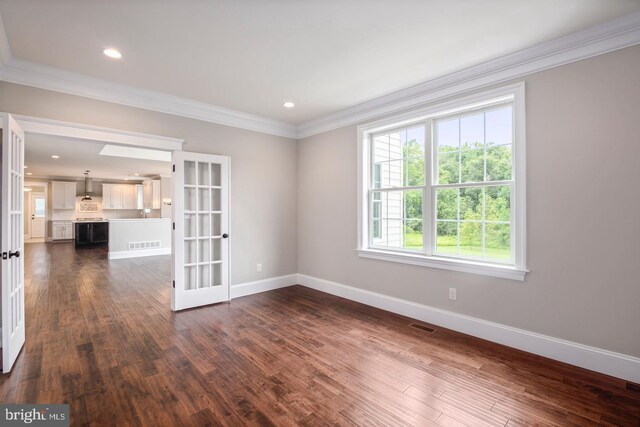 empty room with a wealth of natural light, dark wood-type flooring, and ornamental molding