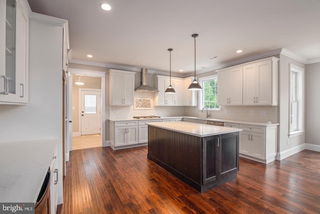 kitchen featuring a kitchen island, white cabinetry, wall chimney exhaust hood, decorative light fixtures, and stainless steel gas stovetop