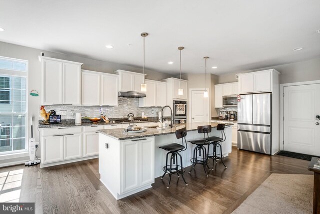 kitchen with light stone counters, dark wood-type flooring, sink, white cabinets, and a center island with sink