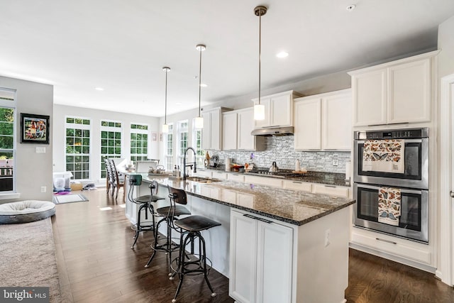 kitchen featuring dark stone countertops, an island with sink, white cabinets, stainless steel appliances, and sink