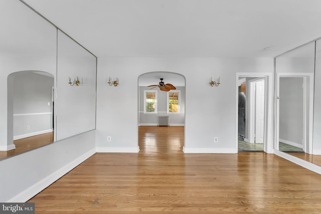 spare room with light wood finished floors, ceiling fan, arched walkways, and baseboards