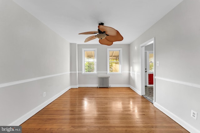 unfurnished room featuring ceiling fan, radiator heating unit, light wood-style flooring, and baseboards