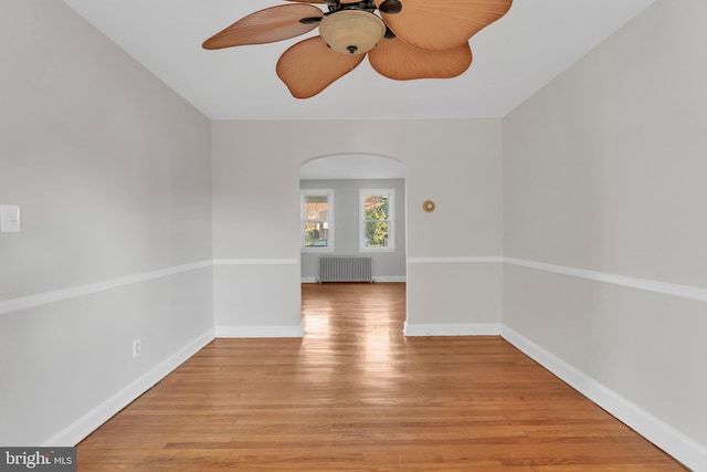 unfurnished room with light wood finished floors, baseboards, arched walkways, radiator, and ceiling fan