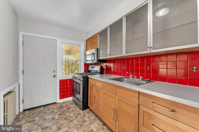 kitchen featuring light floors, stainless steel appliances, light countertops, glass insert cabinets, and a sink