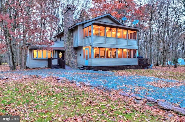 back of house with entry steps, a sunroom, and a chimney