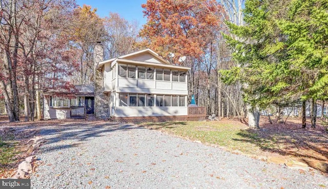 view of front of property with driveway, a sunroom, and a chimney