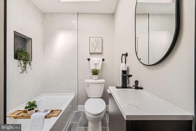 bathroom featuring tiled tub, vanity, and toilet