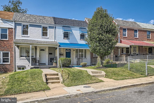 multi unit property featuring covered porch, a shingled roof, a front lawn, and fence