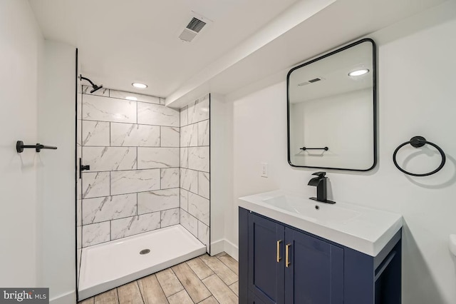 bathroom with wood-type flooring, a tile shower, and vanity