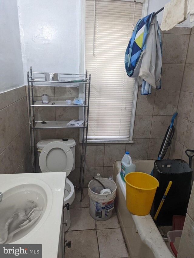 bathroom with toilet, vanity, tile patterned floors, tile walls, and a bath