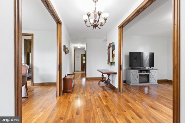 hall featuring light wood-style floors, baseboards, and a chandelier