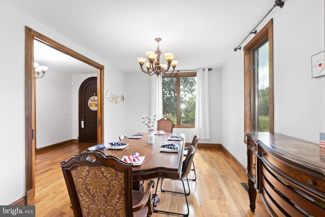 dining room with light wood-type flooring, arched walkways, a notable chandelier, and baseboards