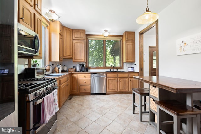 kitchen with a sink, stainless steel appliances, decorative light fixtures, and light tile patterned floors