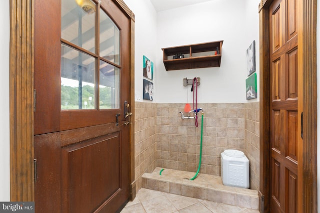 full bath featuring a wainscoted wall, tile walls, a tile shower, and tile patterned flooring