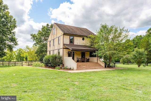 rear view of house featuring a porch, a yard, fence, and stucco siding