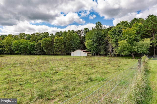 view of yard featuring an outbuilding, a rural view, a detached garage, and fence