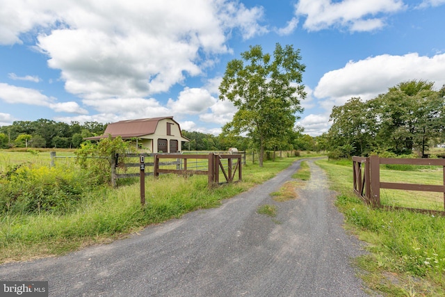 view of road with a gated entry, a rural view, a barn, and driveway