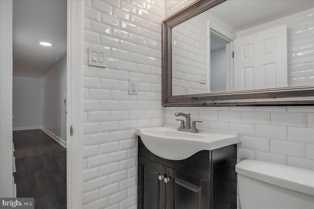 half bathroom with tile walls, baseboards, vanity, and toilet