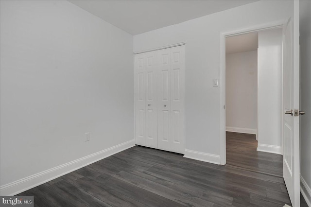 unfurnished bedroom with dark wood-style floors, baseboards, and a closet